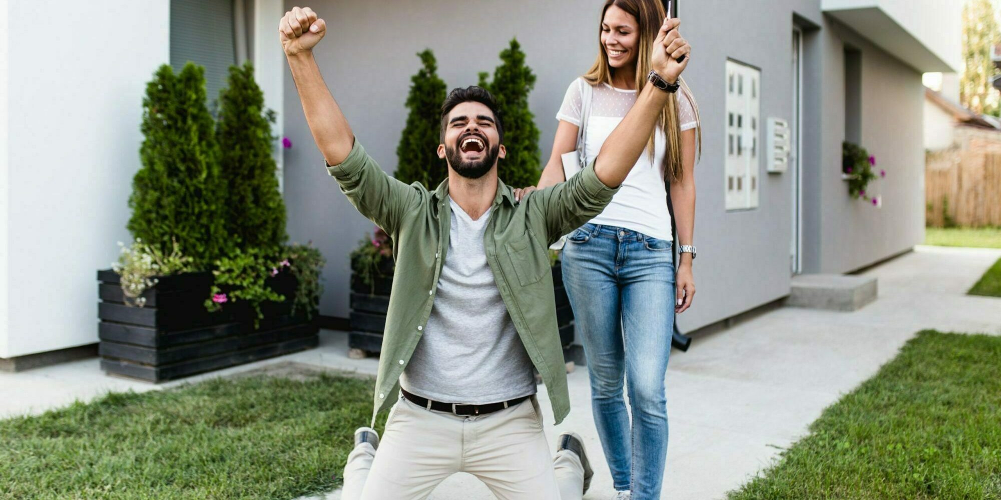 Happy young couple with key standing outside in front of their new home.